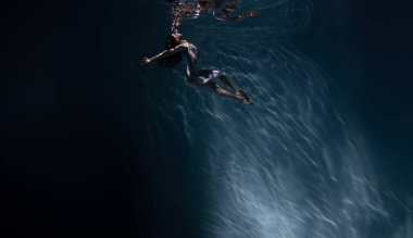 Beyaz elbiseli, su altında yüzen ve güneş ışınları arasında dans eden güzel balerin. Suya karşı balerin..