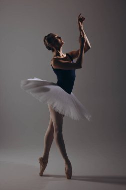 Zarif beyaz etekli genç balerin ve koyu arkaplanda dans eden sivri uçlu ayakkabılar. Zarif, küçük balerin karanlıkta gösteri yapıyor. Bale sanatı, zarafet, esneklik, hareket.