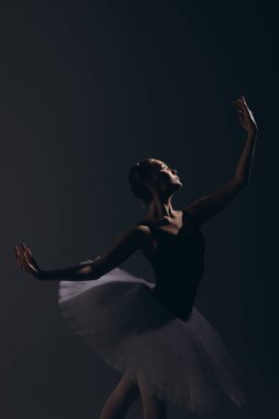 Zarif beyaz etekli genç balerin karanlık arka planda dans ediyor. Zarif, küçük balerin karanlıkta gösteri yapıyor. Bale sanatı, zarafet, esneklik, hareket. Yakın plan..