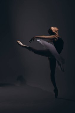 Zarif beyaz etekli genç bir balerin ve siyah arka planda Arabesk pozu veren sivri uçlu ayakkabılar. Zarif, küçük balerin karanlıkta gösteri yapıyor. Bale sanatı, zarafet, esneklik, hareket.