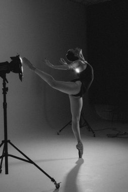 Genç balerin takım elbiseli ve sivri uçlu ayakkabılarıyla sahne ışıklarının arkasında Arabesk pozu veriyor. Zarif, güzel balerin. Bale sanatı, zarafet, esneklik, hareket. Siyah ve beyaz resim.