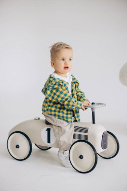 Beyaz arka plana rağmen bir çocuk arabasında oynayan ve ata binen tatlı bir çocuk. Mutlu çocukluk, sevgi ve ilgi.