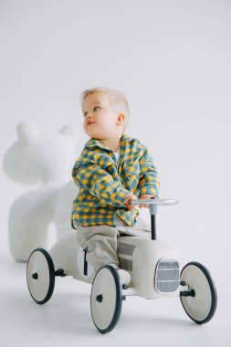 Beyaz arka plana rağmen bir çocuk arabasında oynayan ve ata binen tatlı bir çocuk. Mutlu çocukluk, sevgi ve ilgi.
