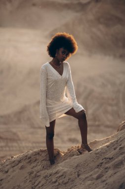 Gün batımında kumlu kanyonda beyaz elbiseli güzel bir Afrikalı kadın. Arka ışıklandırma.