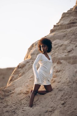 Beyaz elbiseli güzel bir Afrikalı kadın gün batımında kumlu kanyonun arka planında poz veriyor..