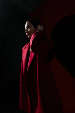Kırmızı ceketli güzel bir kız. Siyah arka planda ışıkla aydınlatılmış..