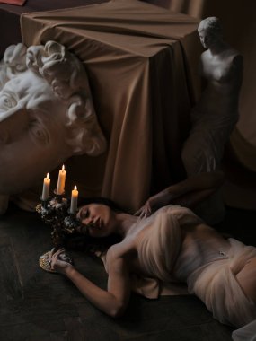 Seksi kadın heykeltıraş atölyede yatıyor ve işten sonra şamdanın yanında antik heykellerin arka planında yanan mumlarla dinleniyor. İlham, hayal gücü ve yaratıcılık için rahatlama.