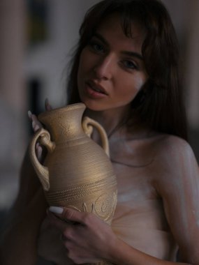 Ellerinde amforo olan ve sanatçı atölyesinde poz veren seksi bir kadın portresi. İlham ve yaratıcılık. Sanatçı atölyesi. Poz modeli.