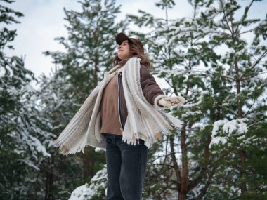 Mutlu, gülümseyen genç bir kadın kış günü karlarla kaplı çam ağaçlarının arasında orman yürüyüşünün tadını çıkarıyor..