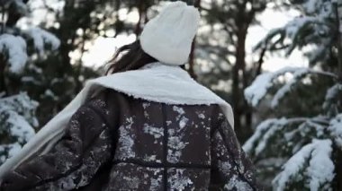 Mutlu, gülümseyen genç bir kadın. Kış ormanlarında, karla kaplı çam ağaçlarının arasında dönüyor ve eğleniyor..