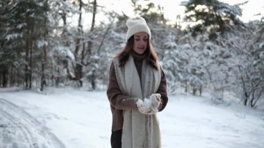 Mutlu genç kadın eğleniyor, kartopları yapıyor ve orman boyunca karla kaplı çam ağaçlarının arasında yürürken yukarı doğru kar fırlatıyor..