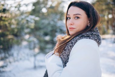 Beyaz önlüklü ve eşarplı esmer kadının portresi kış günü yürüyüş sırasında çam ağaçlarının arasında..