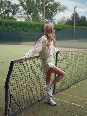 Spor giyim ve güneş gözlüklü genç bayan tenis antrenmanından sonra dışarıda raketin yanında duruyor..