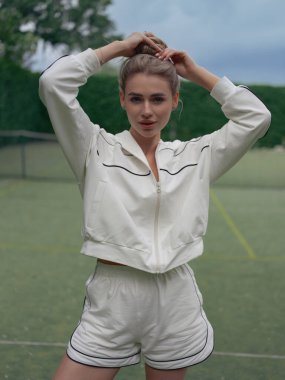 Spor giyim sektöründe genç bir bayan tenis antrenmanından sonra dışarıda dinleniyor ve spor sahasının arka planında poz veriyor. Yakın plan..