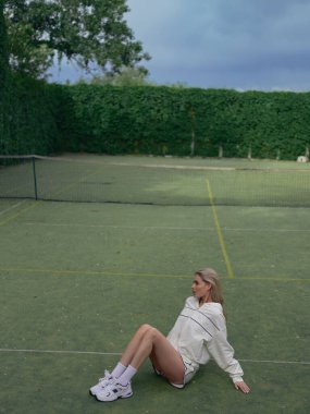 Genç yorgun atletik kadın tenis antrenmanından ve spor sahasında oturduktan sonra dinleniyor. Tenis antrenmanı, aktif eğlence ve sağlıklı yaşam tarzı. Üst görünüm.