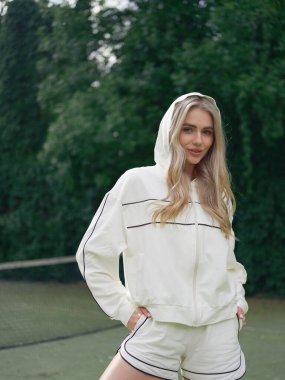 Kapüşonlu ceketli genç atletik kadın tenis antrenmanından sonra spor sahasının arka planında dinleniyor. Yakın plan..