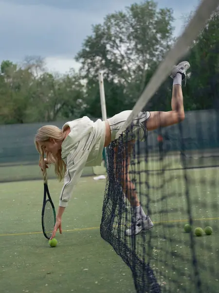 Elinde raketi olan genç bir kadın topa uzanıyor ve top için eğiliyor ve tenis kortunda becerilerini geliştiriyor. Aktif eğlence ve sağlıklı yaşam tarzı.