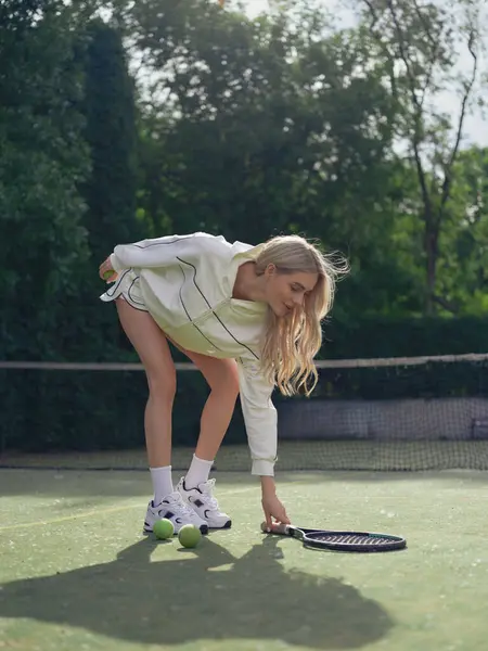 Genç bir kadın tenis kortunda raket eğitip pratik yapmak için eğiliyor. Tenis eğitimi, aktif eğlence ve sağlıklı yaşam tarzı..