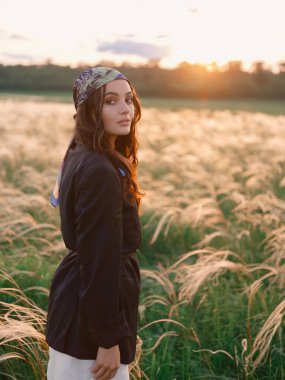 Gün batımında bozkırda tüylü otların arasında yürüyen genç bir kadın güzel manzaraya karşı. Ukrayna 'da bozkırda tüy çimenli yaz manzarası. Arka ışıklandırma. Yakın plan..