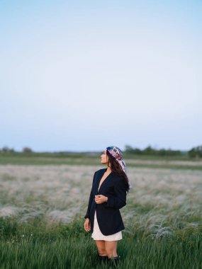 Genç bir kadın, bozkırda, mavi gökyüzü olan güzel manzaraya karşı tüy otlarının arasında duruyor ve dinleniyor. Ukrayna 'da bozkır çimenli yaz manzarası.