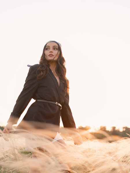 Young woman walking among feathergrass in steppe at sunset against sky background. Summer outdoor scene with feather grass in steppe in Ukraine. Backlit and close-up. Bottom view.