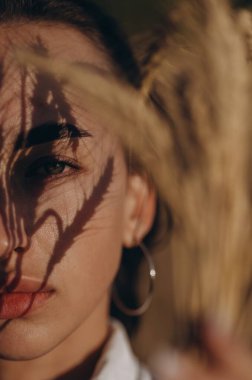 Yüzünde buğday buğdayından yapılmış gölgesi olan güneş ışığı almış genç bir kadının yarım portresi. Kırsal yaz manzarası, doğal güzellik. Yakın plan..