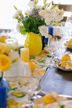 Limonlar, beyaz çiçekler, mumlar ve zarif sofra takımlarıyla süslenmiş şık bir yemek masası. Taze çiçekli süs, kırsal ama modern tasarım. Yaz kutlaması ya da düğün ziyafeti.