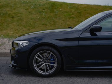 Şehir caddesine park edilmiş parlak siyah sedan 'ın ön tarafına bakın. Modern tasarım, parlak dış görünüş, şık detaylar ve güçlü varlık. Lüks araç zarafeti, hızı ve karmaşıklığı simgeliyor.