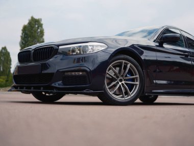 Yakın çekim tarafı ve parlak, modern koyu mavi sedanın alt tarafı. Fotoğraf, ızgarayı, farları ve araba tekerleğini ön plana çıkarıyor..