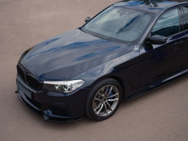 Parlak, modern koyu mavi sedan 'ın yakın çekim üst görüntüsü. Fotoğraf, ızgaraları, farları, araba kaputunu ve tekerleği vurguluyor..