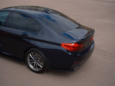 Sokakta park etmiş koyu mavi bir sedan. Parlak tasarım, stop lambaları ve yansımalı parlak boya. Arabanın arka kısmı. Otomotiv görüntüleri için mükemmel.