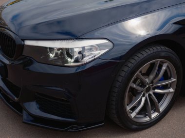 Modern koyu renkli sedanın ön tarafını gösteren yakın plan fotoğraf. Parlak far, şık alaşımlı tekerlek ve parlak boyaya odaklan. Otomotiv tasarımı ve teknoloji temaları için ideal.