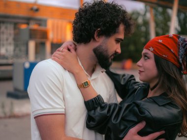 Birbirlerini kucaklayan, gözlerinin içine bakan genç bir çift. Duygusal günbatımı sahnesi iki insan arasındaki romantik ilişkiyi ve mahrem anı gösteriyor..