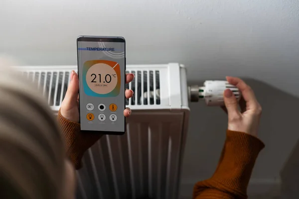 Smartphone with launched application for air temperature adjustment opposite the radiator. Health microclimate at home concept.