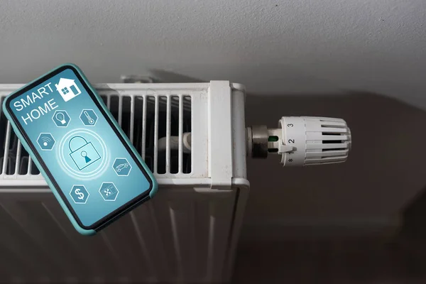 Smartphone with launched application for air temperature adjustment opposite the radiator. Health microclimate at home concept.