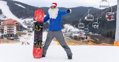 Kayak merkezinde kar kayağı yapan Noel Baba şapkalı bir adam.