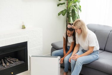 Anne ve çocuk elektrikli ısıtıcının yanında ellerini ısıtıyorlar.