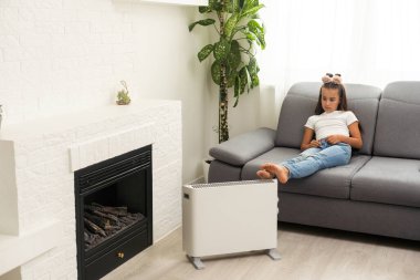 little girl near the heater, thermostat. Energy crisis.