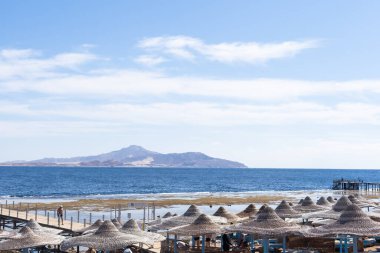 Kumsalda güneşli yatakları ve saman güneş şemsiyeleri olan Akdeniz kıyıları.