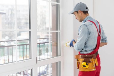 Yakışıklı genç adam yeni bir inşaat alanına pencere takıyor.