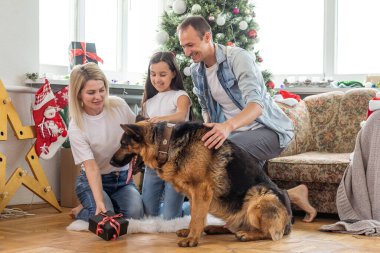 Gülümseyen aile ve kız ve köpek Noel ağacının yanında hediyelerle oturuyor..