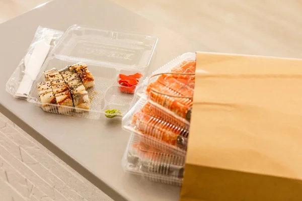 白いテーブルの上に紙パックの近くのプラスチック製の箱に寿司ロール 配達だ Take Away — ストック写真