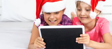 Heyecanlı küçük kardeş çocuklar modern tablet aletleriyle oynarken eğleniyorlar. Mutlu küçük kız çocukları ped cihazıyla video izleyip, kış tatillerinde evde eğleniyorlar.