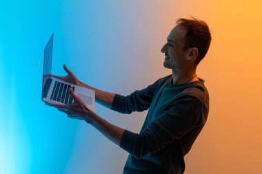 Çekici, neşeli, neşeli, başarılı, başarılı, zeki, esmer adam, emlakçı adamın portresi. Dizüstü bilgisayarını tutuyor, renkli arka plan üzerinde çalışıyor..