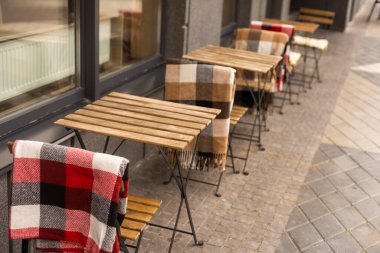 Gri çimento zemin üzerinde sokak kafesinde battaniyeli masa ve sandalyeler. Yaşam tarzı, eğlence, içki, dışarıda yemek konsepti, romantik..