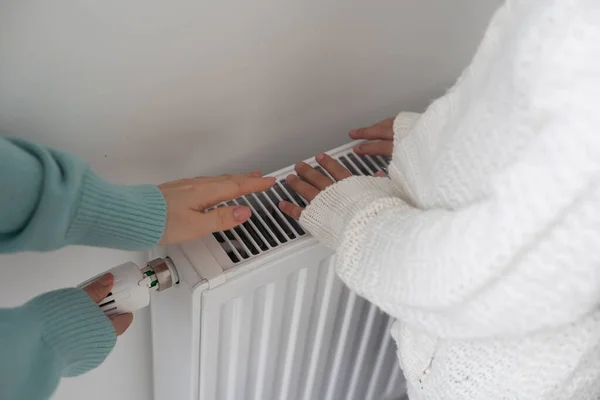 Child warming hands on heating radiator near white wall, closeup.