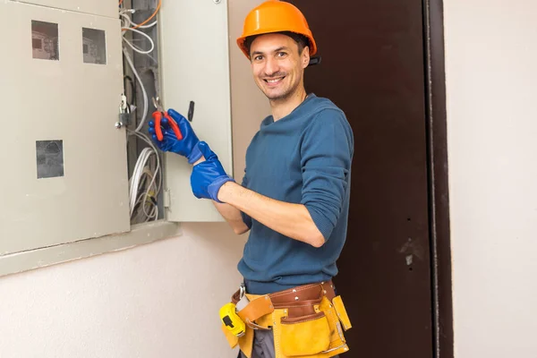 Close up shot of hand of aged electrician repairman in uniform working, fixing, installing ethernet cable in fuse box, holding flashlight and cable. hand and cable.
