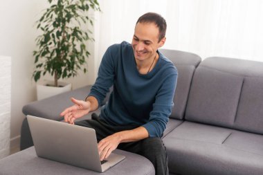 Genç erkek kullanıcı elinde dizüstü bilgisayarla kanepede dinleniyor. Boş beyaz ekranı taklit ediyor. Modern defter sörfü, haber okumak, online çalışma kavramı kullanan bir adam.