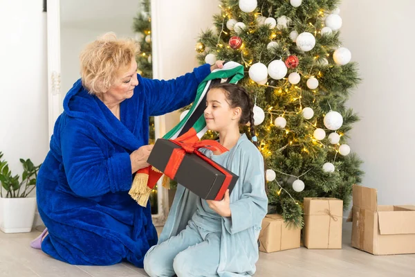 Kış tatili ve aile kavramı - mutlu büyükanne ve torun evde noel ağacının yanında bayraklı.