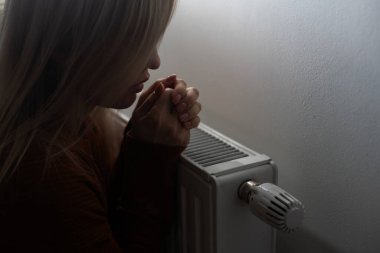 Closeup of woman warming her hands on the heater at home during cold winter days, top view. Female getting warm up her arms over radiator. Concept of heating season, cold weather.